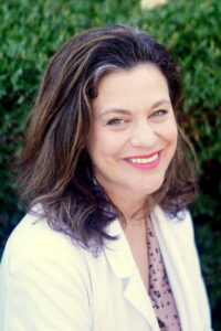 Smiling woman with brown hair wearing a white jacket.